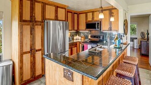Una cocina con armarios de madera, electrodomésticos de acero inoxidable, encimeras de granito e iluminación colgante.