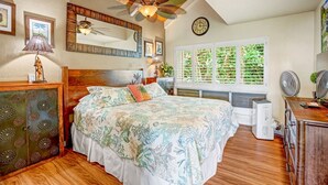 Un dormitorio con cama, techo de madera, ventilador de techo, ventana con contraventanas y un reloj en la pared.