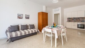 A compact living space with a sofa, dining table, chairs, a cabinet, and a kitchen area.