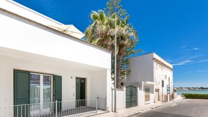 A coastal building with a white facade, green shutters, and a balcony with a metal railing.