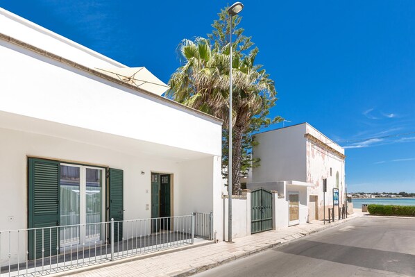 A coastal building with a white facade, green shutters, and a balcony with a metal railing.