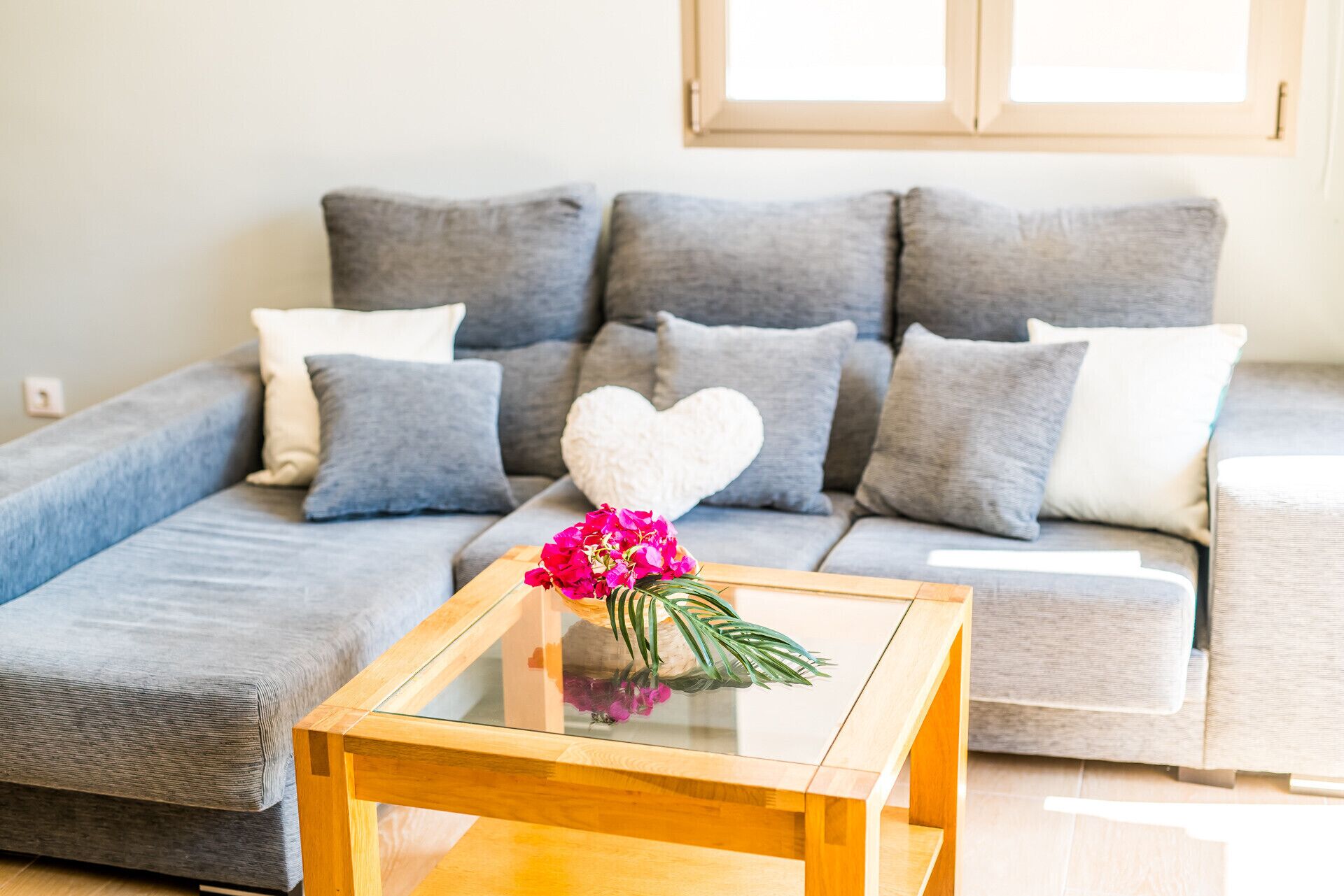 A living room with a grey sofa, a glass coffee table, and a heart-shaped decoration.