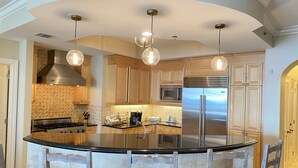 Una cocina moderna con una isla central, electrodomésticos de acero inoxidable e iluminación colgante.