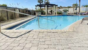 Una piscina con borde de baldosas, una pérgola y palmeras al fondo.