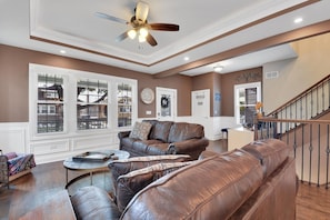 A spacious living room with a brown leather sofa set, a coffee table, and a ceiling fan.