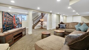 Ein geräumiges Wohnzimmer mit einer großformatigen Stadtansicht als Wandgemälde, einer Treppe und einer gemütlichen Sitzecke mit Sofa und Hocker.
