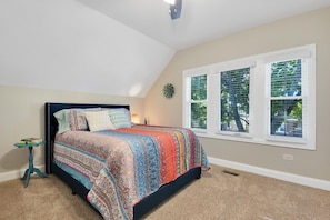 A bedroom with a large bed, a small table, and a window with blinds.