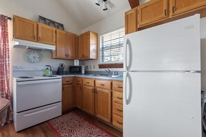 Compact kitchen with a stove, sink, refrigerator, and microwave, plus a clock and window with blinds.