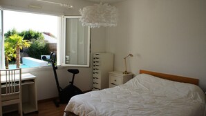 A bedroom with a bed, a desk, a chair, a treadmill, a wardrobe, and a window with a view of a pool and greenery. - Beautiful 160m² Villa with Heated Pool in Perigny (Perigny)