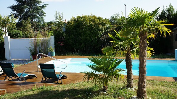 Relax by the serene pool surrounded by lush greenery and a wooden deck.