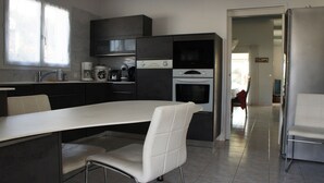 A modern kitchen with a central island, built-in appliances, and a dining area with a white table and chairs. - Beautiful 160m² Villa with Heated Pool in Perigny (Perigny)