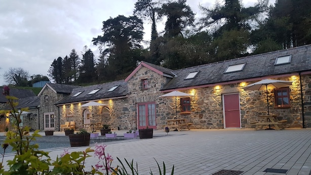 A stone building with a red door, outdoor seating, and a paved courtyard. - Cobbles Cottage - 2 Bedroom Stone Built Cottage (Ballynahinch)