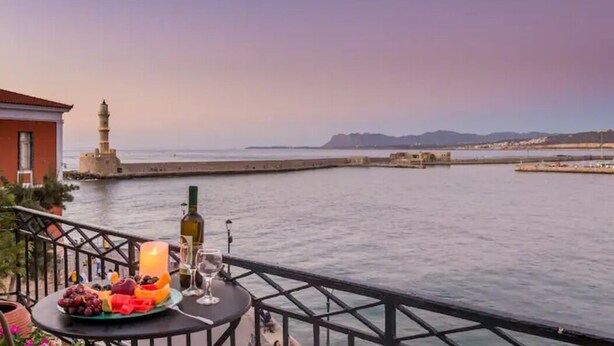 Een balkon met een tafel gedekt voor een maaltijd, met uitzicht op water en een afgelegen vuurtoren.