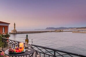 Un balcon avec une table dressée pour un repas, donnant sur une étendue d’eau et un phare situé au loin.