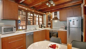 Een moderne keuken met houten kastjes, een roestvrijstalen koelkast, een magnetron en een eettafel met een schaal fruit en een glas sap.