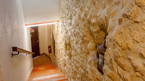 Een trap met rode strepen die leidt naar een kamer met een stenen muur en een hangende lamp.