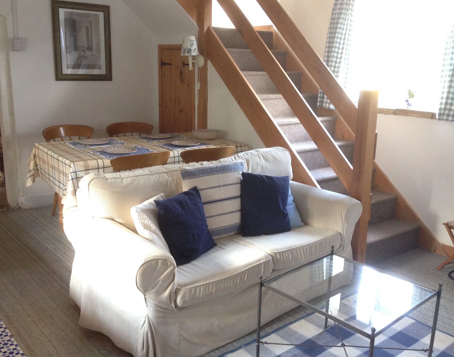 A living room with a sofa, a glass coffee table, a dining table with chairs, and a staircase.