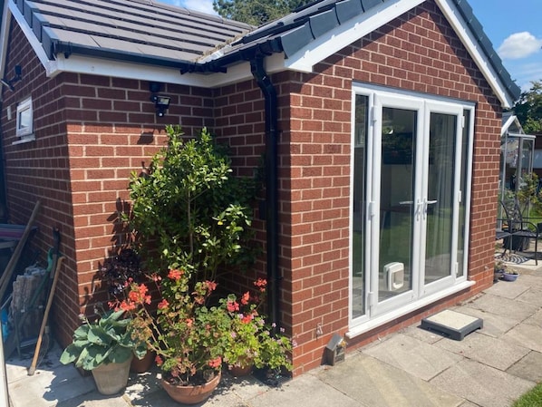 A brick house with a glass door and a small garden with potted plants. - Rose View - Modern Detached Bungalow (Sale)