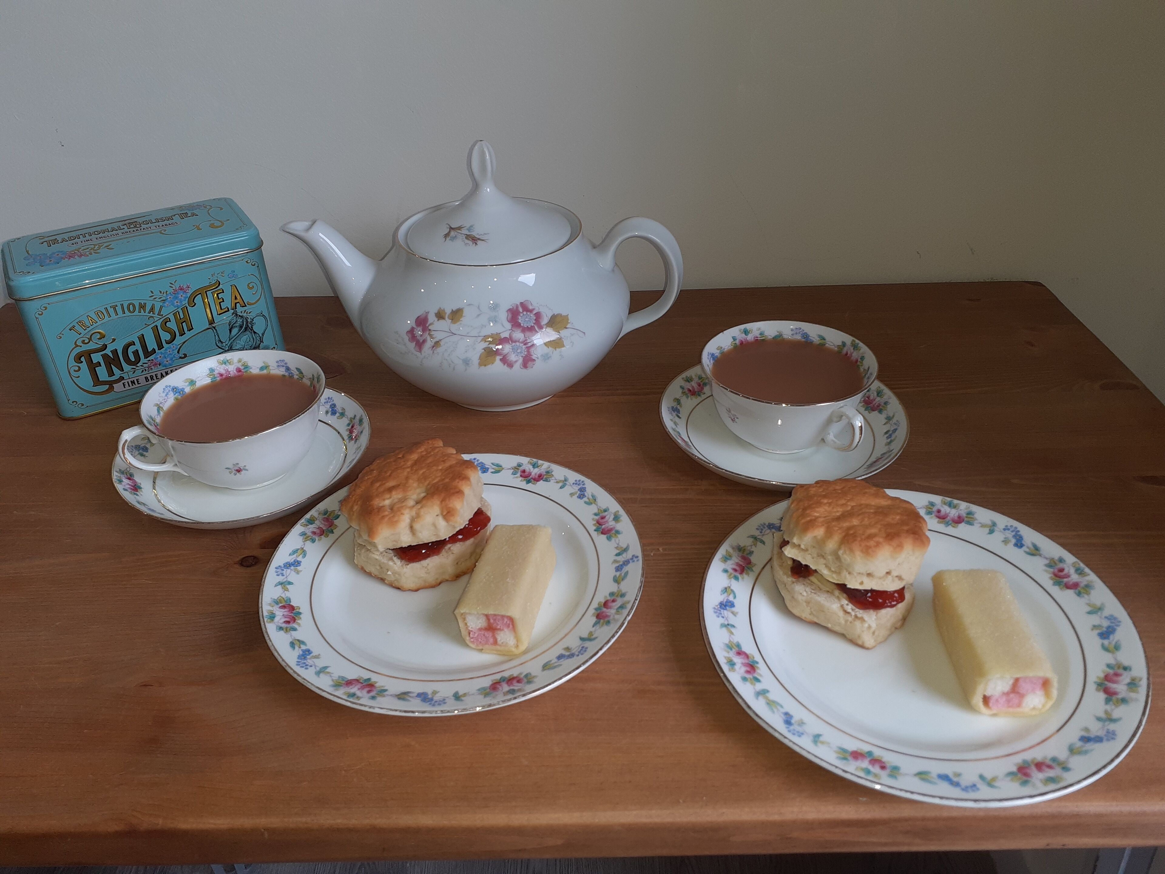 A table with a teapot, two cups of tea, and two plates with scones and jam.