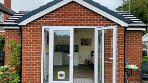 Une petite maison de plain-pied, avec une façade en briques et une porte-fenêtre à cadre blanc qui donne sur un espace cuisine.
