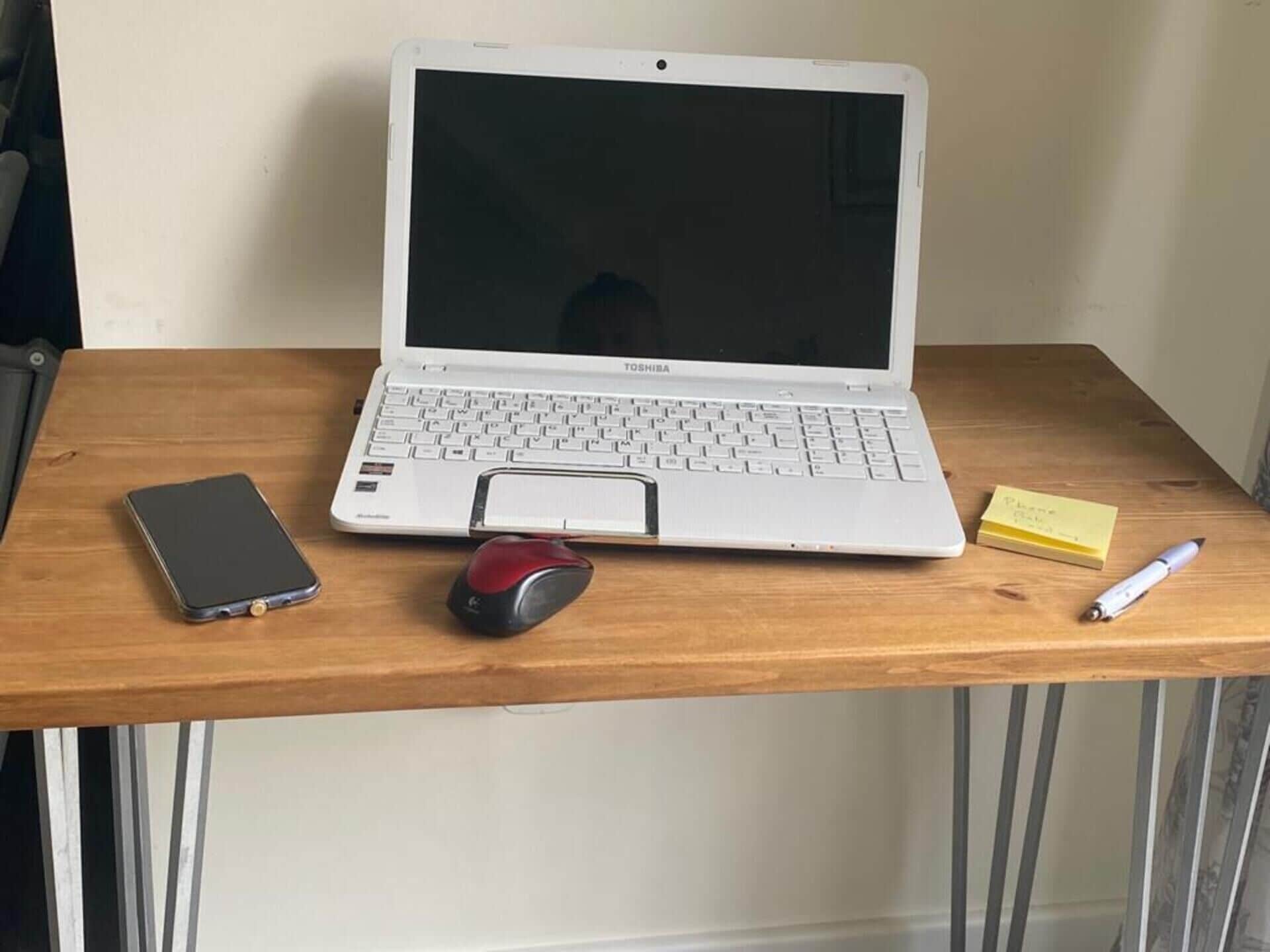A laptop on a wooden desk with a smartphone, a mouse, sticky notes, and a pen.