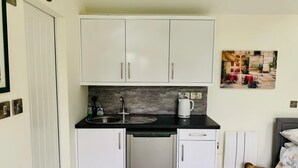 Una cocina compacta con gabinetes blancos, una encimera negra, un lavavajillas de acero inoxidable y una cafetera.