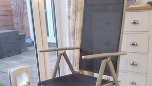 Una habitación con una silla plegable, un aparador blanco y una ventana que da a vistas del exterior.