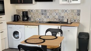 A compact kitchen with a dining area, including a washing machine, a coffee maker, and a microwave.