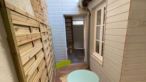 A narrow wooden deck with a round table and two chairs, a wooden fence, and a door leading to an interior space.