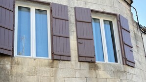 A building with multiple windows and shutters, stone walls, and a door.