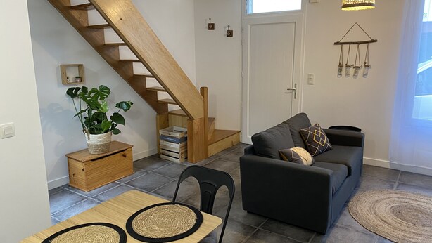 A living room with a wooden staircase, a sofa, a dining table with two placemats, and a hanging light fixture.