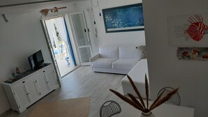 A modern living room with a white sofa, a flat-screen TV on a cabinet, and a dining area with a table and chairs.