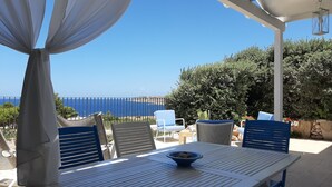 A terrace with a table and chairs, overlooking a coastal view.