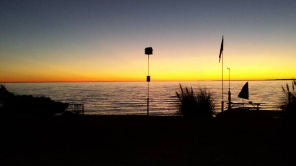 Escena de playa con un atardecer, un asta de bandera y una bandera.