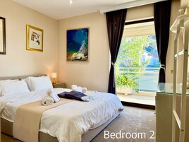 A bedroom with two beds, a large window with a view, and artwork on the walls.