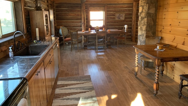 L’intérieur d’un chalet rustique comprend une cuisine, un coin repas et une cheminée en pierre.