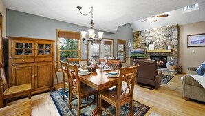 A dining area with a wooden table and chairs, a chandelier, and a stone fireplace. - Dollywood Close, Near Pkwy, Hot Tub, Grill, Arcade (Pigeon Forge)