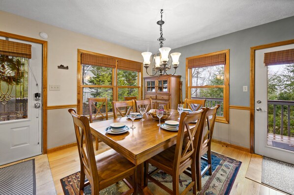 A dining room with a wooden table set for six, flanked by wooden chairs, a chandelier, and a cabinet with glass doors.