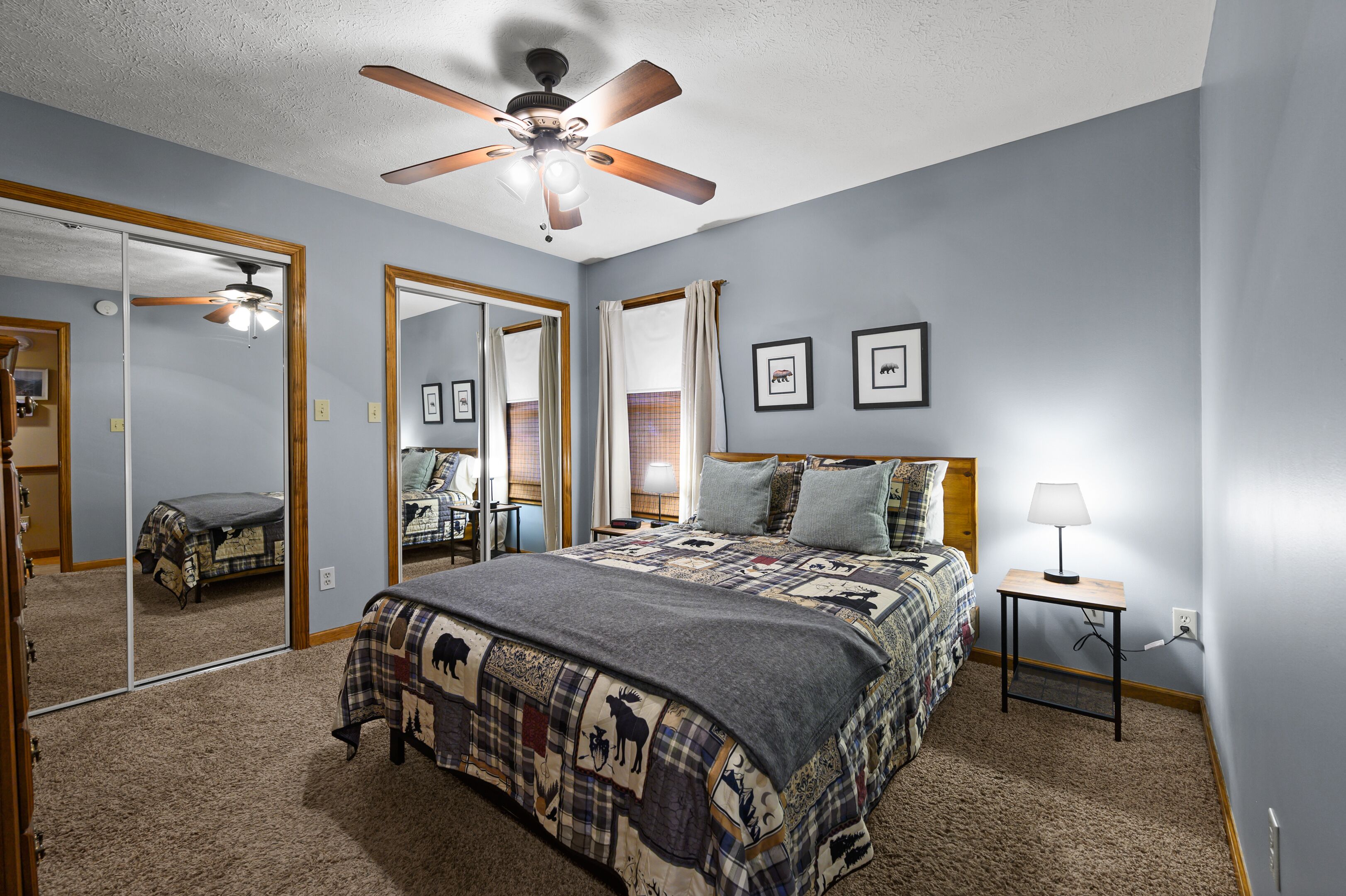 A bedroom with a bed, a ceiling fan, a nightstand, and a mirror.