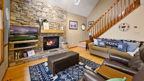 A living room with a stone fireplace, a television, a sofa, and a staircase. - Dollywood Close, Near Pkwy, Hot Tub, Grill, Arcade (Pigeon Forge)
