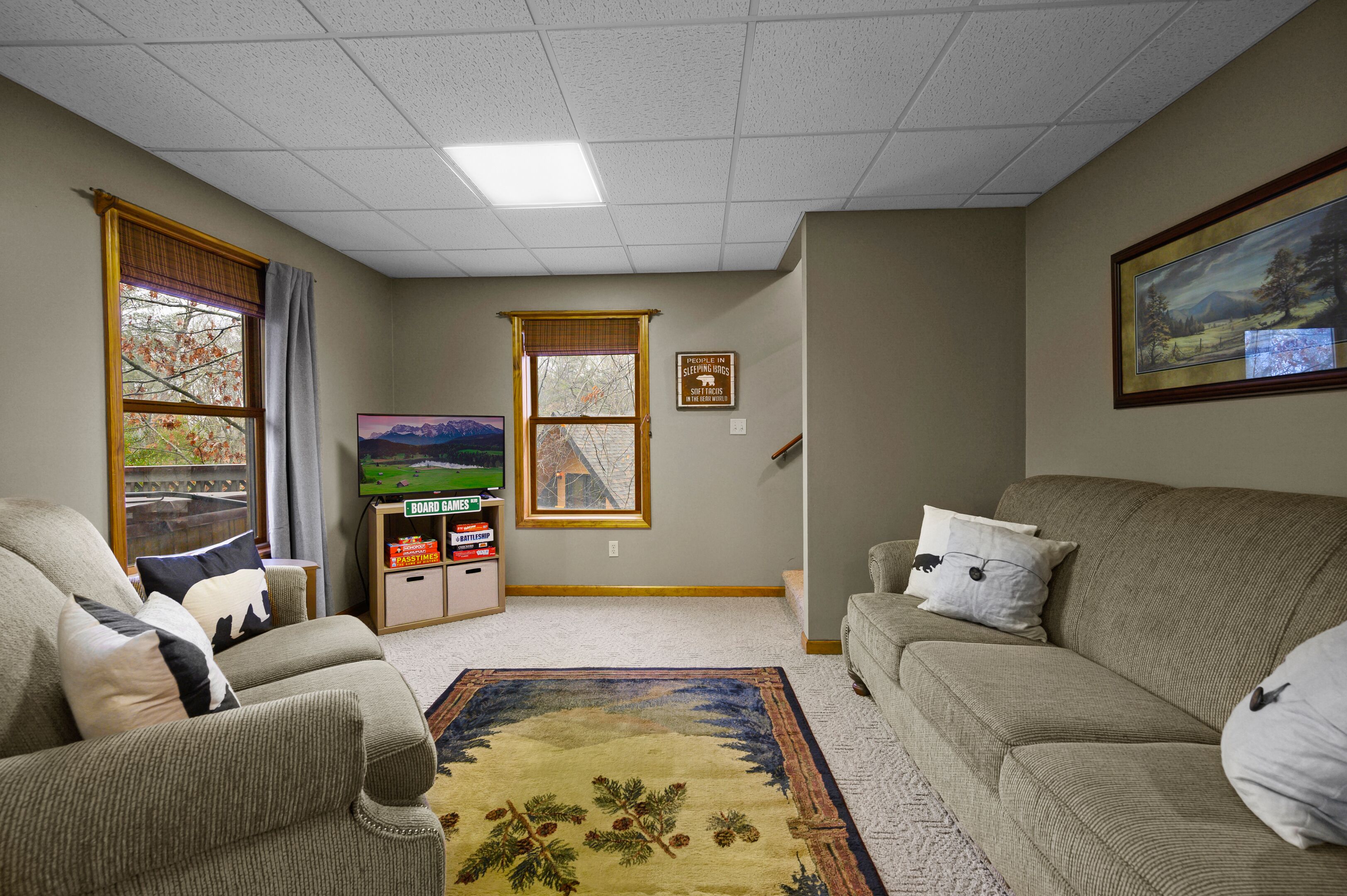 A living room with a sofa, a television, a bookshelf, and a window with a view of trees.