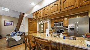 A kitchen with wooden cabinets, a stainless steel refrigerator, a granite countertop, and a dining area with a wooden table and chairs. - Dollywood Close, Near Pkwy, Hot Tub, Grill, Arcade (Pigeon Forge)