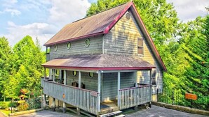 A two-story wooden house with a porch, a steeply pitched roof, and a small front yard. - Dollywood Close, Near Pkwy, Hot Tub, Grill, Arcade (Pigeon Forge)