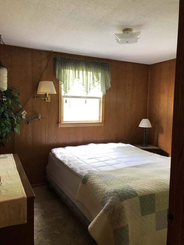 Un dormitorio con una cama individual, una mesita de noche, una lámpara, una ventana con cortina y una luz en el techo.