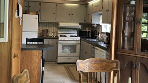 A kitchen with wooden cabinets, a stove, a microwave, and a dining area with a table and chairs. -  Reduced to $90.00 March-July week days (Byrnedale)