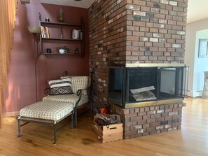 Un salon chaleureux avec une cheminée en briques, un banc en bois et une bibliothèque adossée à un mur rouge.