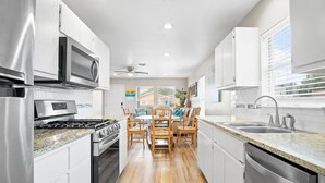 Una cucina moderna con mobili bianchi, elettrodomestici in acciaio inossidabile, un tavolo da pranzo in legno con sedie e vista su case attraverso ampie finestre.
