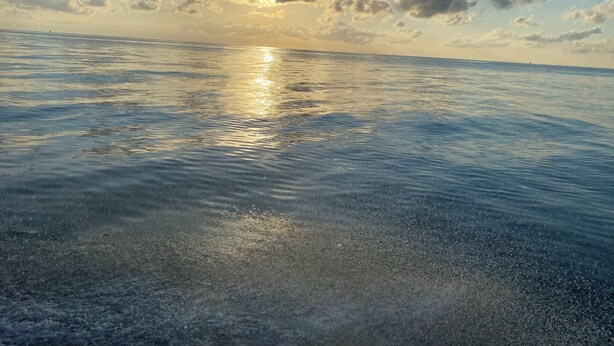 Mare calmo con il sole che si riflette sulla superficie e cielo sereno con nuvole sparse.