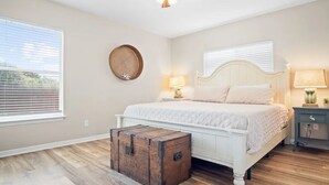 Una camera da letto con un letto bianco, pavimento in legno, una ventola a soffitto, un comodino con una lampada e uno specchio rotondo fissato alla parete.