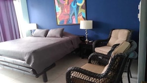 A hotel room with a bed, a chair, a nightstand, and a painting on the wall.